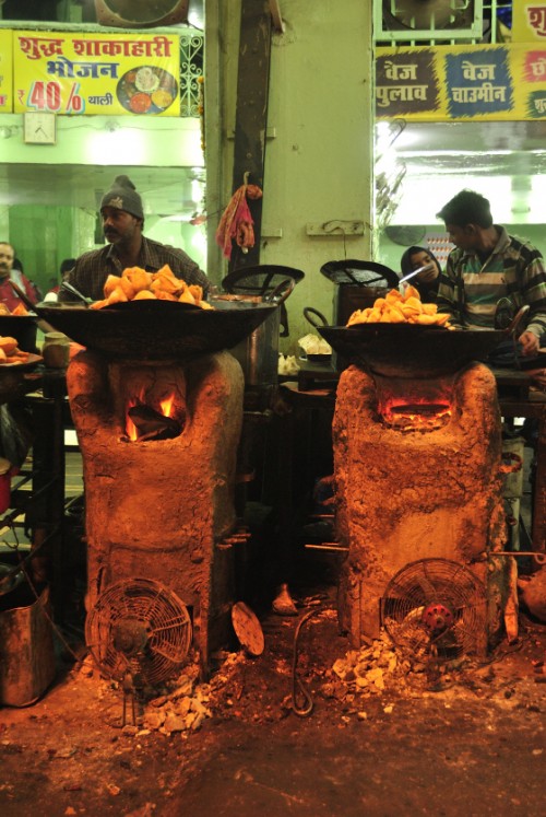 The cooks using huge ladles to get the piping hot samosas and kachoris from the wok, and then resting the ladle on the sides to let the excess oil/ghee drain out. The fire is stoked by table fans – saves on manual labour.