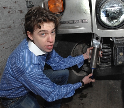 Zack Anderson, senior in electrical engineering and computer sciences, holds a GenShock prototype up to a Humvee coil spring where it is installed. Photo: Donna Coveney.