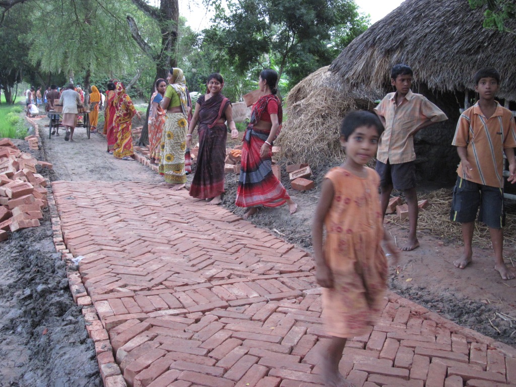 Lotika Sarkar, 23, who could not reach a health centre for an institutional delivery due to lack of connectivity, now energetically guides her friends in laying bricks for the road. (Credit: Saadia Azim\WFS) 