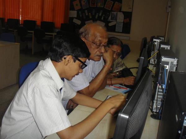 A student helps a senior citizen learn how to use a computer.