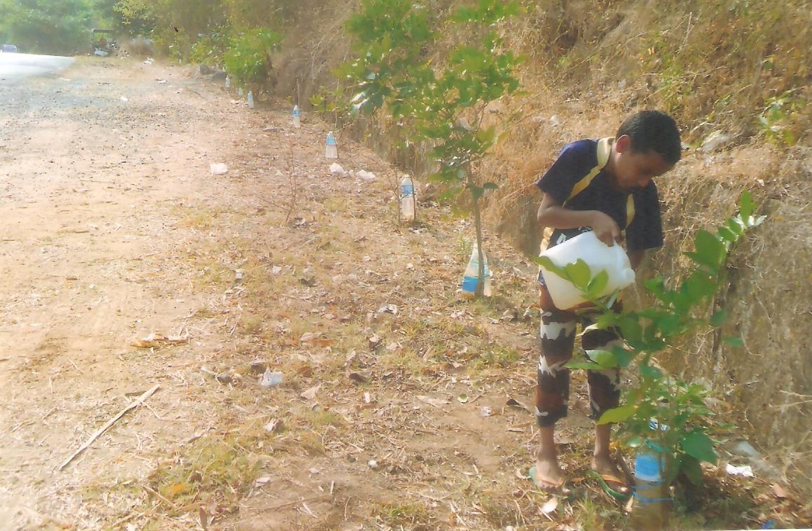 His son helping him to refill water in the bottle tied to young trees