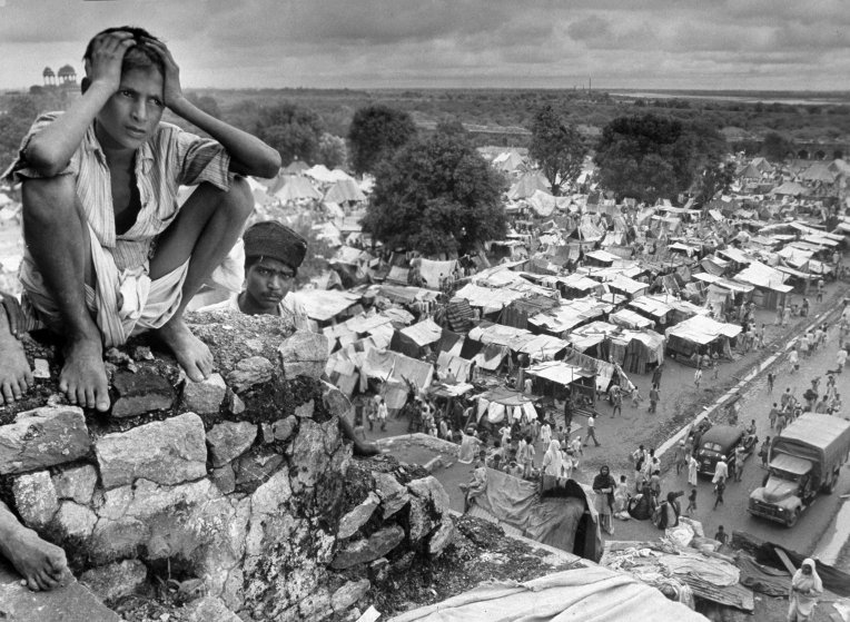 Boy sitting on rock ledge above refugee camp.