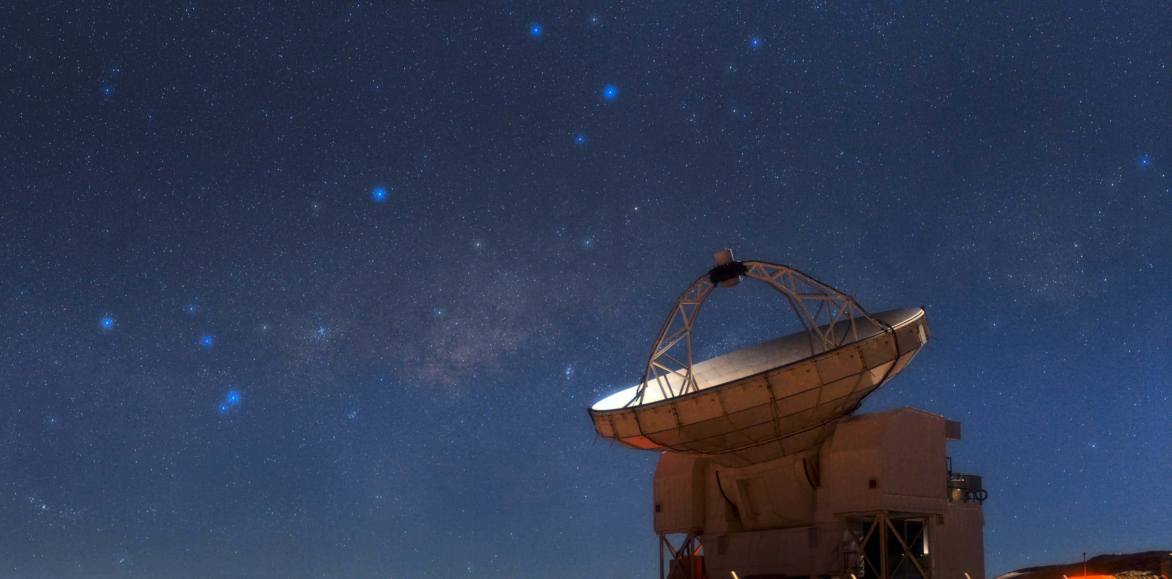 The Atacama Pathfinder Experiment (APEX) telescope looks skyward during a bright, moonlit night on Chajnantor, one of the highest and driest observatory sites in the world. Astronomical treasures fill the sky above the telescope, a testament to the excellent conditions offered by this site in Chile’s Atacama region. On the left shine the stars that make up the tail of the constellation of Scorpius (The Scorpion). The scorpion’s “stinger” is represented by the two bright stars that are particularly close to each other. Reaching across the sky and looking like a band of faint, glowing clouds is the plane of the Milky Way. Between Scorpius and the next constellation to the right, Sagittarius (The Archer), which looms over APEX’s dish, a sparkling cluster of stars can be clearly seen. This is the open cluster Messier 7, also known as Ptolemy’s Cluster. Below Messier 7 and slightly to the right is the Butterfly Cluster, Messier 6. Further to the right, just above the edge of APEX’s dish, is a faint cloud which looks like a bright smudge. This is the famous Lagoon Nebula (see eso0936 for a closer view). With a primary dish diameter of 12 metres, APEX is the largest single-dish submillimetre-wavelength telescope operating in the southern hemisphere. As the telescope’s name suggests, it is blazing a trail for the biggest submillimetre observatory in the world, the Atacama Large Millimeter/submillimeter Array (ALMA), which will be completed in 2013 (eso1137). APEX will share space with the 66 antennas of ALMA on the 5000-metre-high Chajnantor plateau in Chile. The APEX telescope is based on a prototype antenna constructed for the ALMA project, and it will find many targets that ALMA will be able to study in great detail. ESO Photo Ambassador Babak Tafreshi made this panorama using a telephoto lens. Babak is also the founder of The World At Night, a programme to create and exhibit a collection of stunning photographs and time-lapse videos of the world’s most beautiful and historic sites against a nighttime backdrop of stars, planets and celestial events. More information APEX is a collaboration between the Max-Planck-Institut für Radioastronomie (MPIfR), the Onsala Space Observatory (OSO), and ESO, with operations of the telescope entrusted to ESO. ALMA, an international astronomy facility, is a partnership of Europe, North America and East Asia in cooperation with the Republic of Chile. ALMA construction and operations are led on behalf of Europe by ESO, on behalf of North America by the National Radio Astronomy Observatory (NRAO), and on behalf of East Asia by the National Astronomical Observatory of Japan (NAOJ). The Joint ALMA Observatory (JAO) provides the unified leadership and management of the construction, commissioning and operation of ALMA. Links Information about APEX ESO Photo Ambassadors   #L