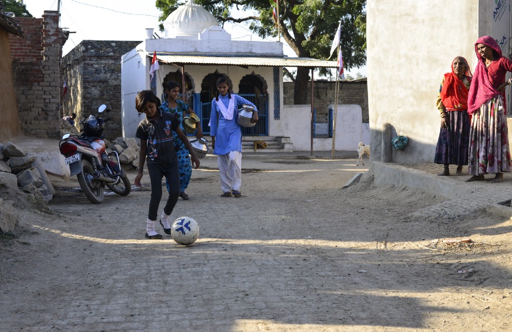 12 year old Monica patting the ball while Nisha and Sonia go to fetch water from a nearby well, in Sakariya village.