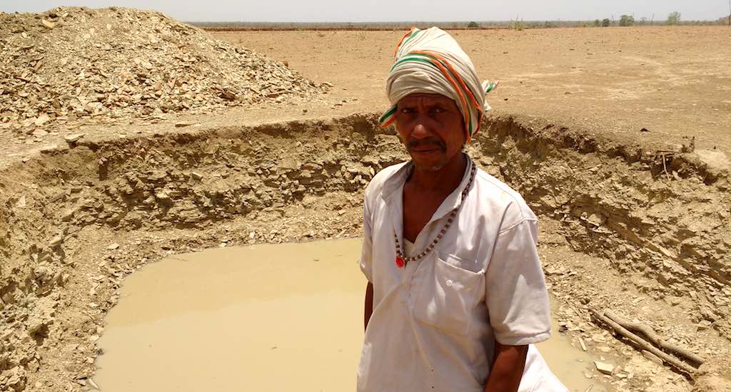 Pooran Adivasi near his farm pond with some water, even as the rest of the landscape wears a parched look. (Photo by Nachiket Sule)