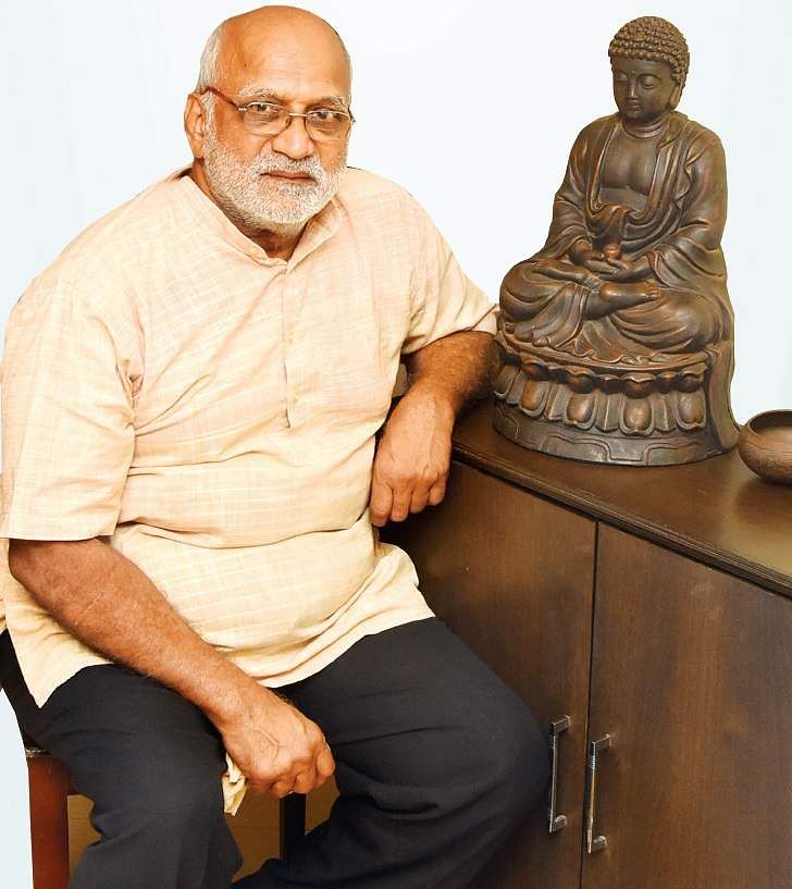 Dr Ravindranath sitting on a chair near a buddha statue 