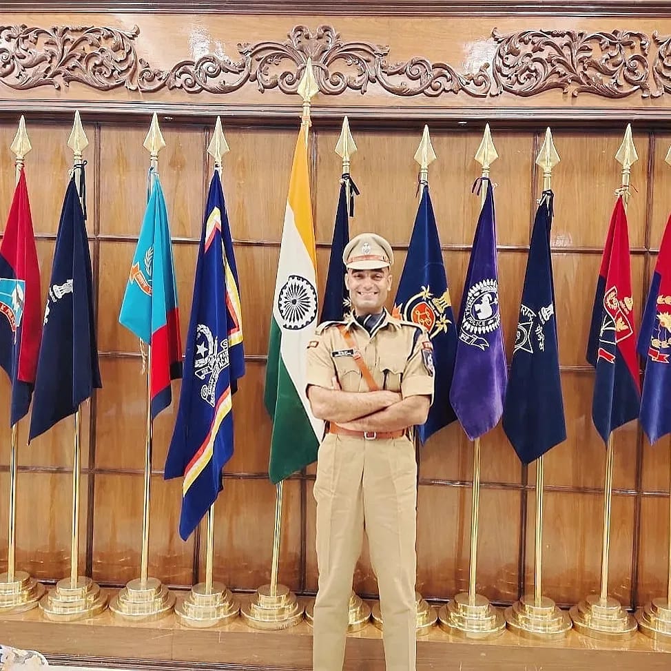 Himanshu Gupta IPS Officer standing amidst flags. 