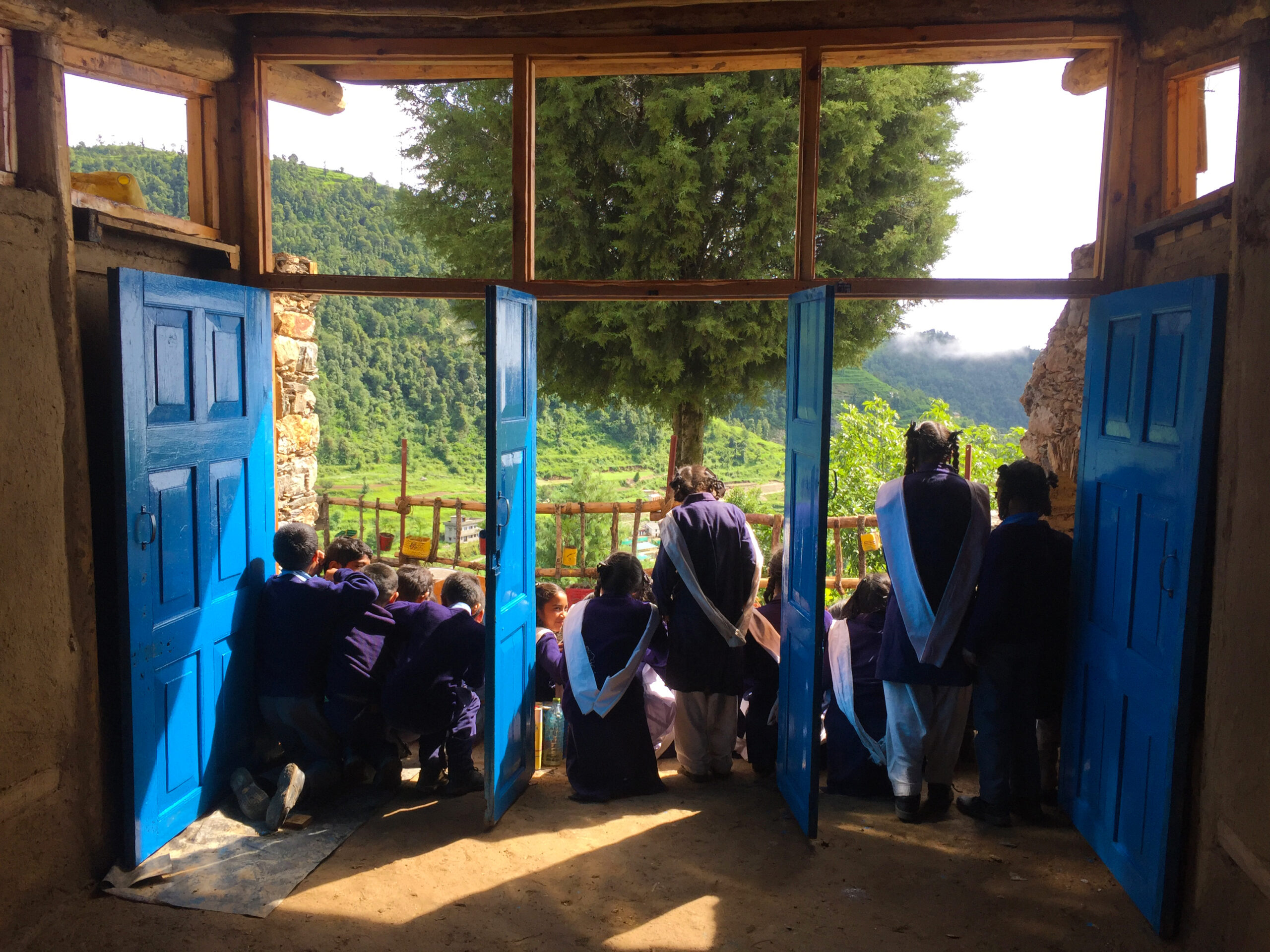 children dressed in school uniforms stand near blue doors 