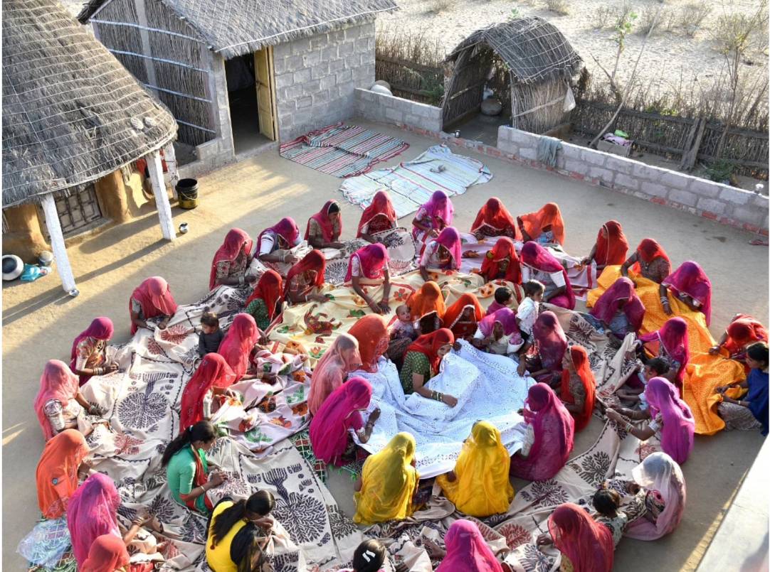 artisan ruma devi embroiders a bed sheet with other women artisans in barmer, rajasthan