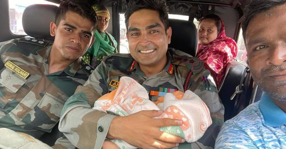 Army officers who rescued a 6 day old infant hold the child and smile