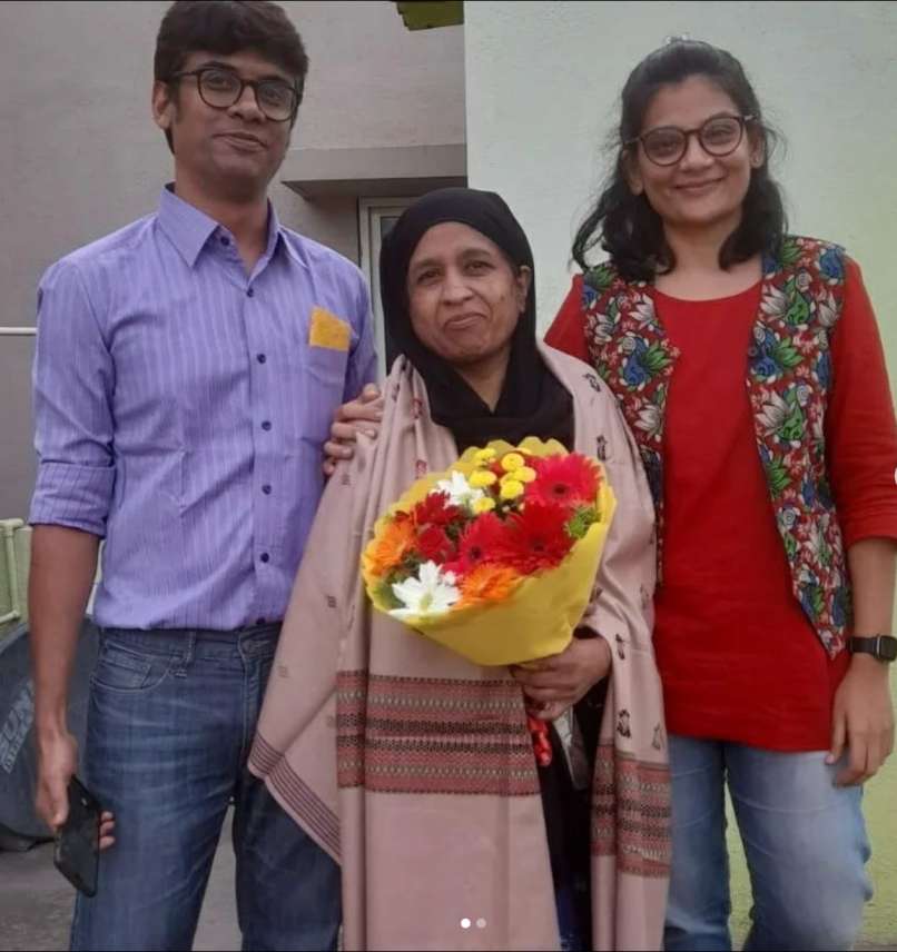 A man and two women, with one holding a bouquet of flowers. 