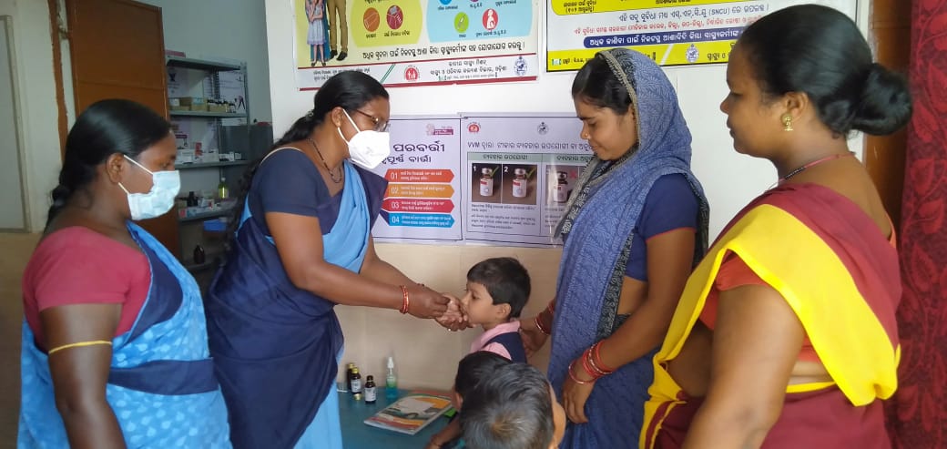 ASHA worker matilda kullu wears a mask as she administers polio drops to a child in a clinic 