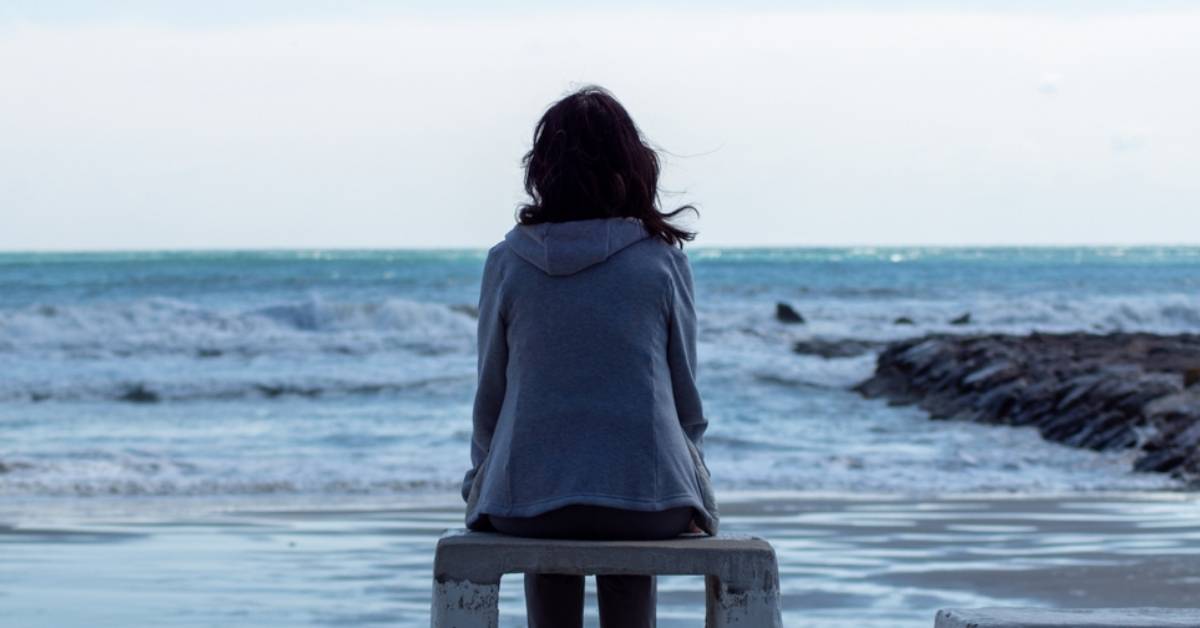 woman with her back turned to camera sits on a beach