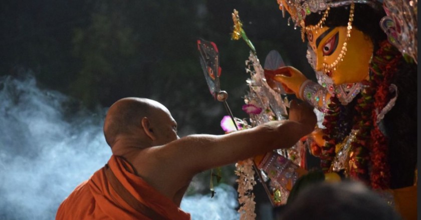 a priest in saffron clothing touches a tall durga idol during durga puja in kolkata