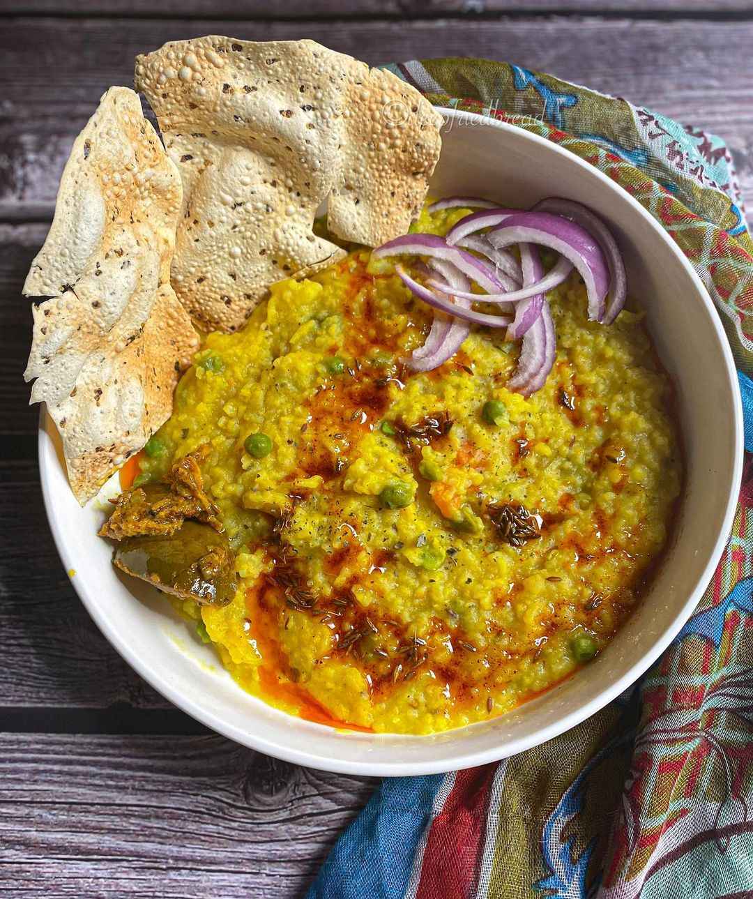 A bowl of khichdi made with rice, moong daal, with papad and onions