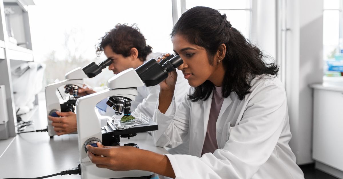a research student looks at a microscope in a lab
