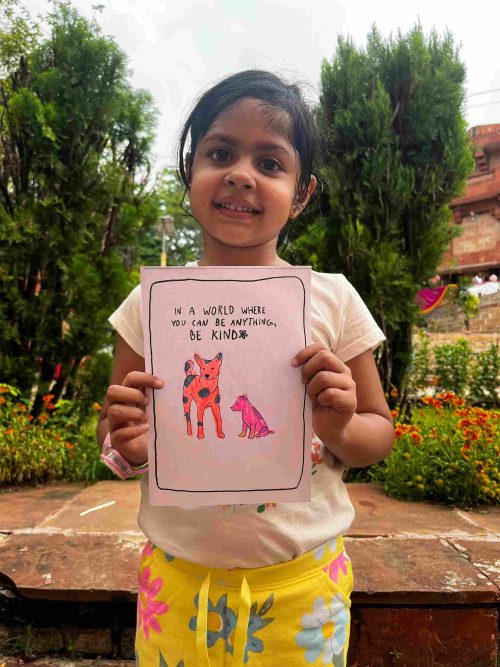 Children holding an artwork that reads, 'In a world where you can be anything, choose to be kind,' promoting kindness and empathy.