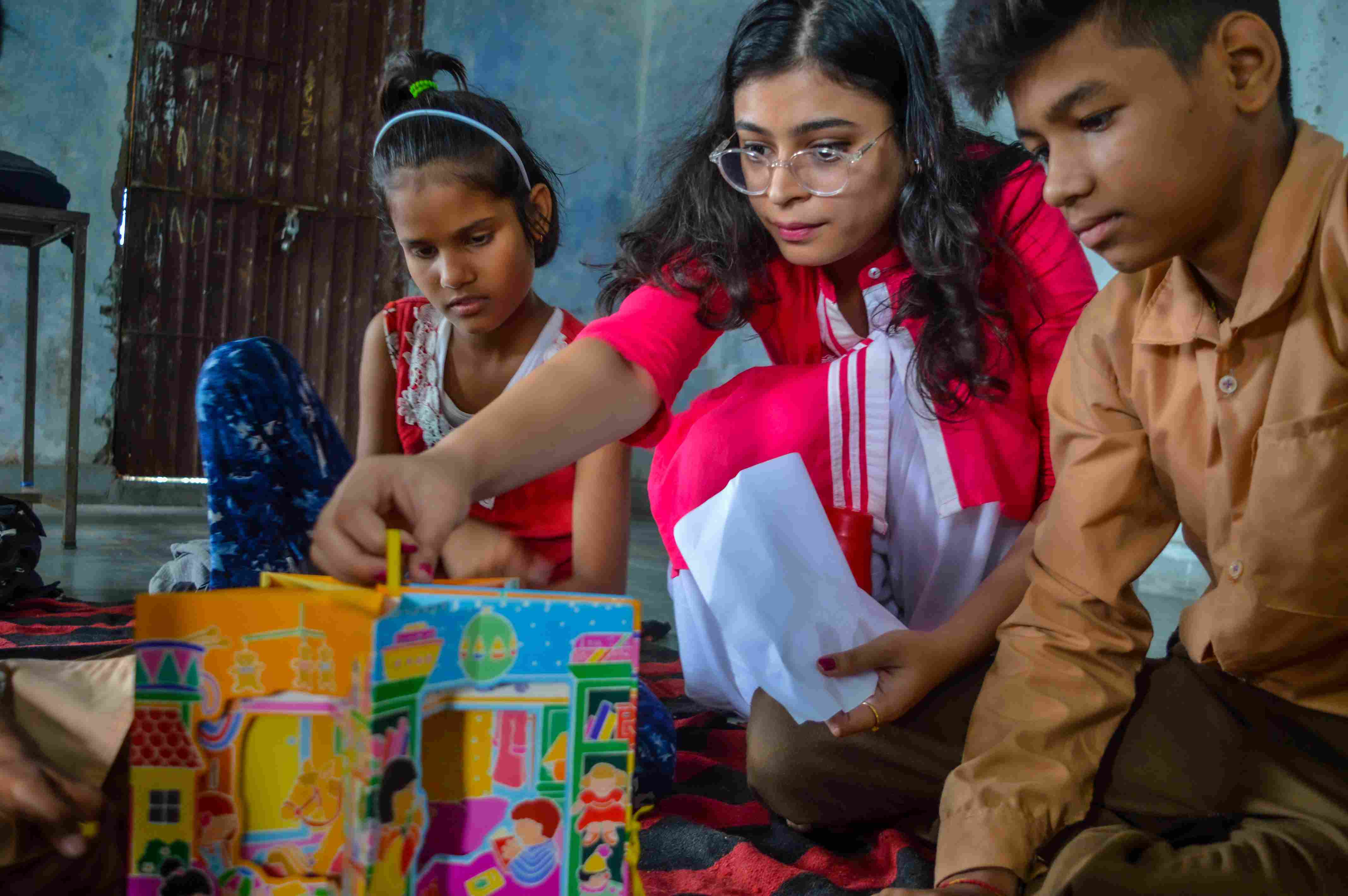 Srishti working closely with two children, teaching them with the help of pop-up books.