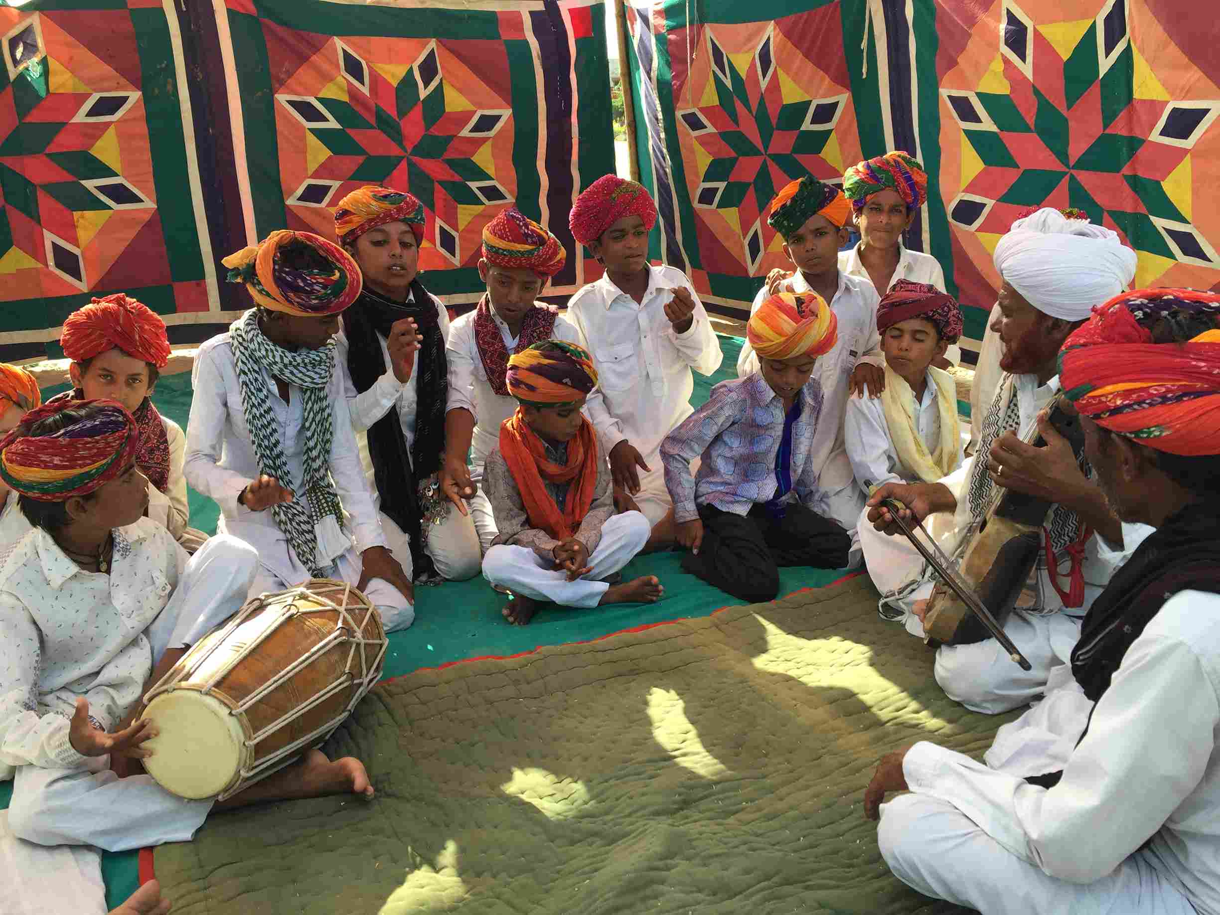 An experienced Rajasthani folk artist teaching young children the intricacies of traditional music at the Lok Sangeet Shala residency, promoting cultural preservation and knowledge transfer.