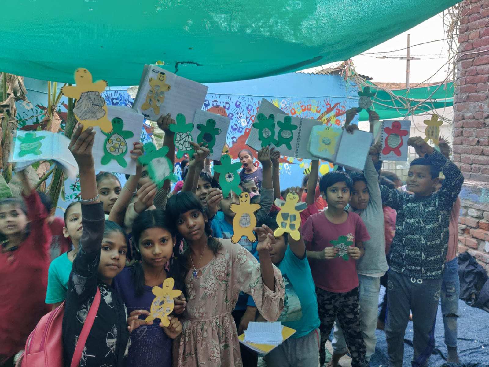 A group of children proudly holding up their drawings, created with the help of SABIA volunteers, showcasing their creativity and talent.