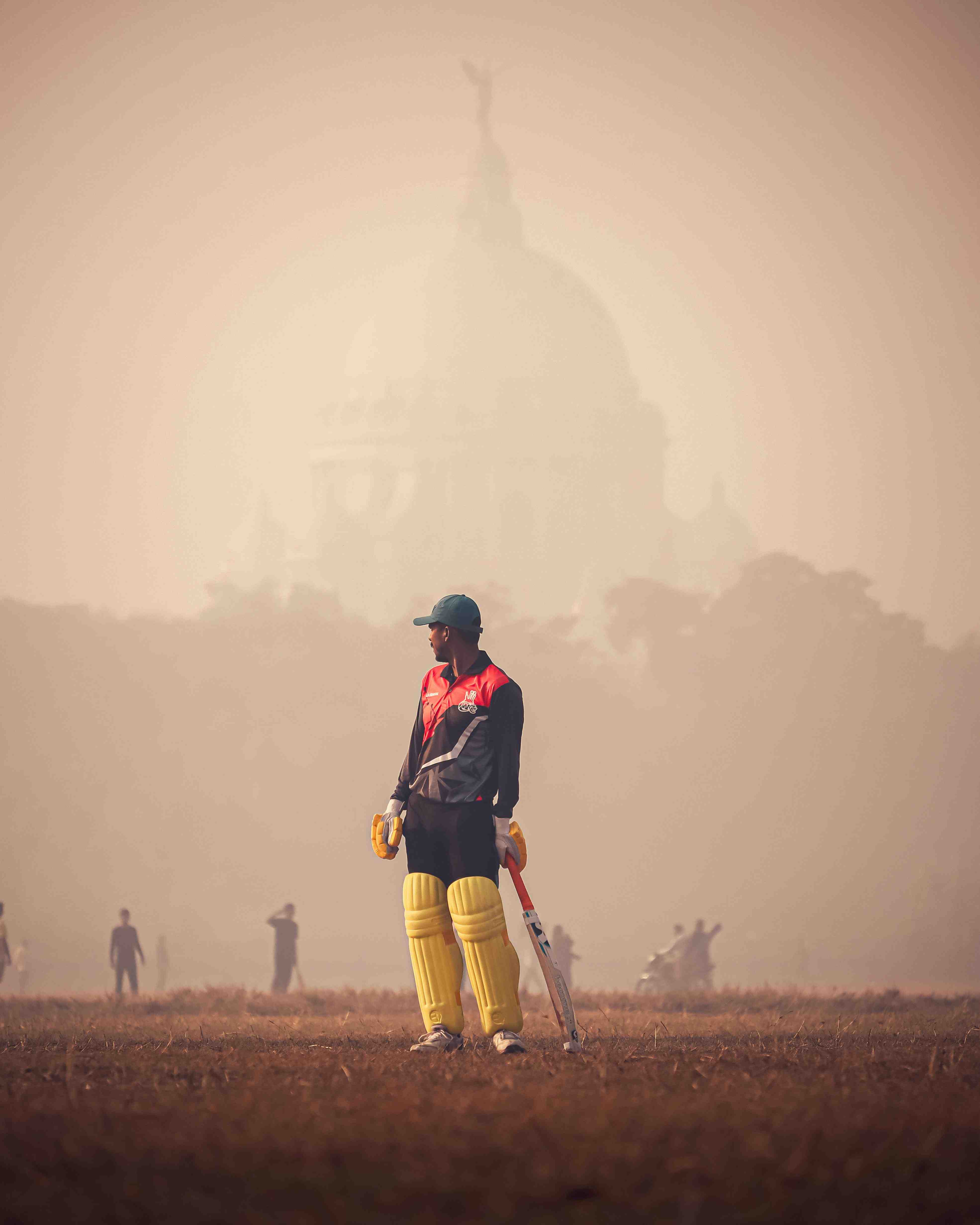 A cricket player on a field obscured by heavy smog and air pollution, reducing visibility.