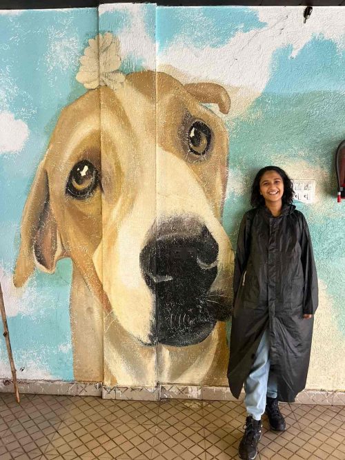 Mouli posing with her mural work she did for a hostel in Rishikesh. 