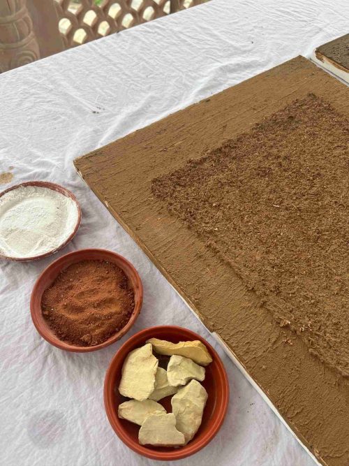  A table displaying a bowl of brown powder alongside a bowl of white powder, and pieces of charcoal with an unfinished artwork on the side. 