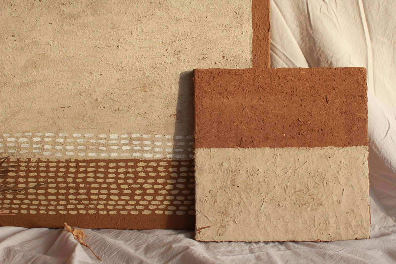 Two colourful clay pieces displayed, showcasing a unique painting made from soil, white charcoal and cow dung.