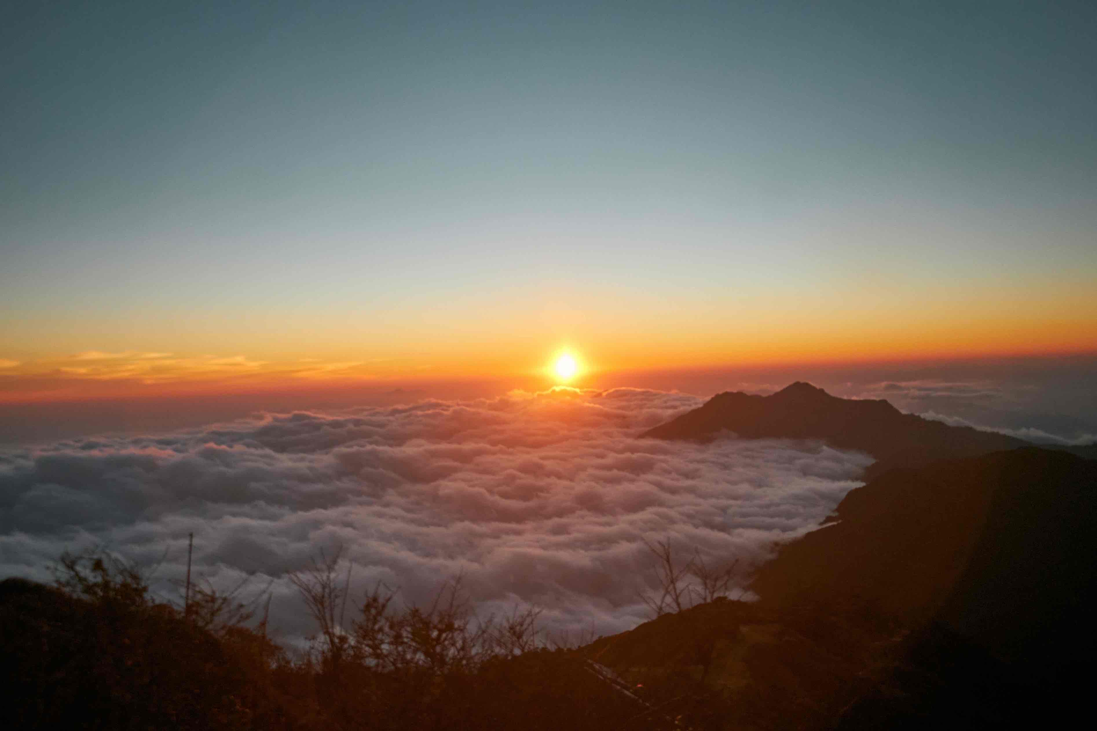 The sun illuminates clouds as it sets in Sandakphu