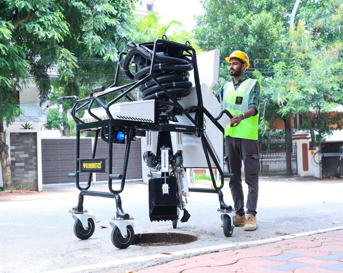 Sanitation worker operating the Bandicoot robot to inspect and clean a manhole with a display screen showing real-time footage.