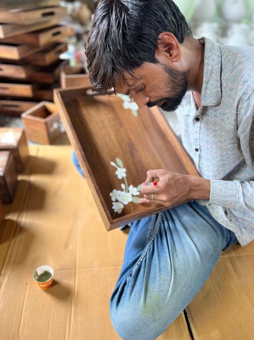 A painter at carefully paints a wooden box adorning it with colourful flowers, showcasing his artistic skills and creativity.