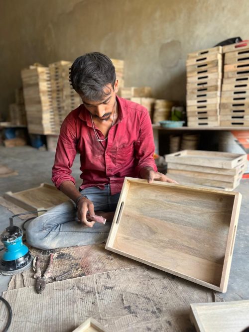 An employee meticulously crafting a wooden tray in a well-equipped workshop, surrounded by tools and materials.